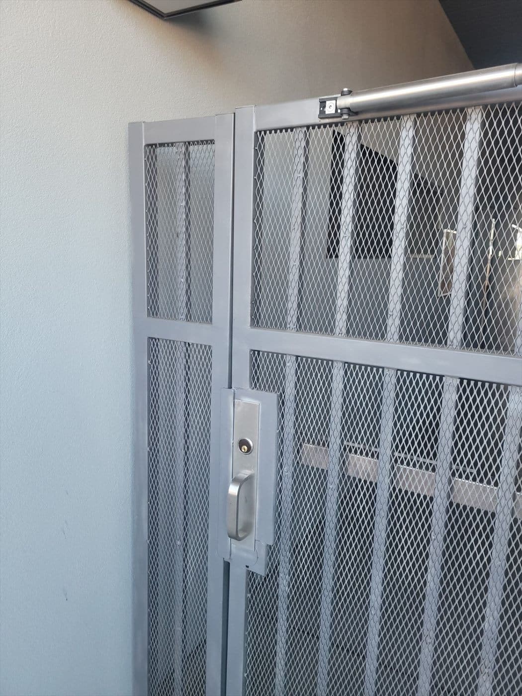 Close-up of a repainted gray expanded-metal security gate with lock and closer.