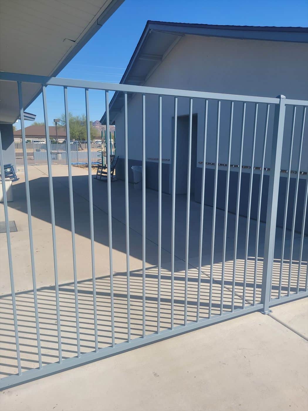 Light blue-gray painted fence enclosing a concrete patio area beside the building.