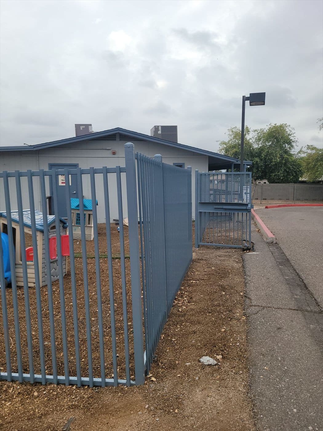 Blue-gray fence enclosing a playground area beside the school on an overcast day.