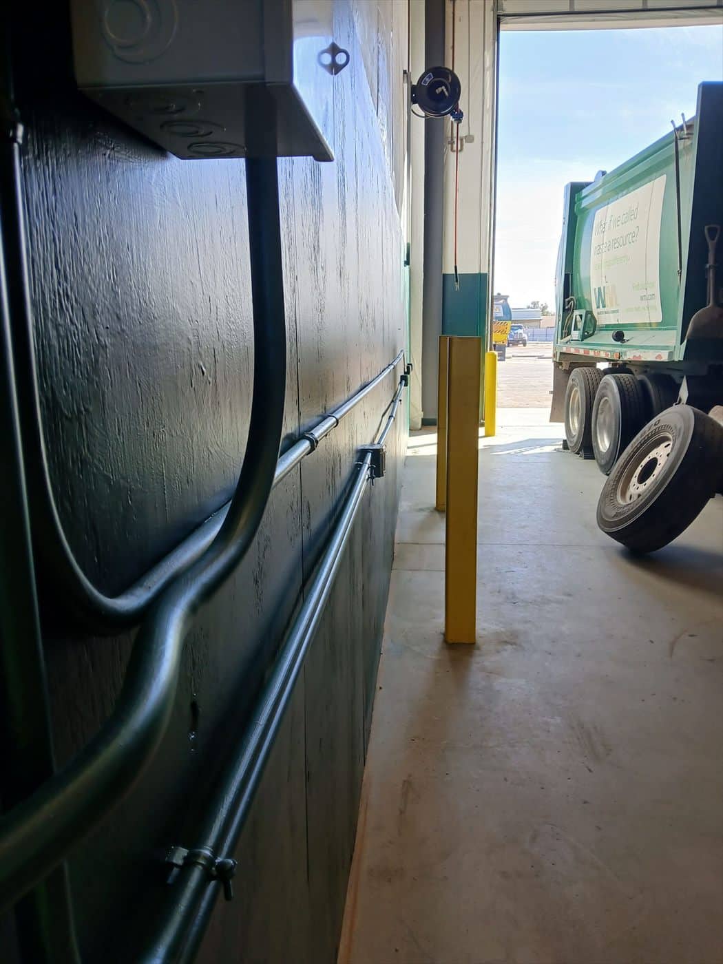 Painted green shop wall with conduit beside an open bay door and truck.