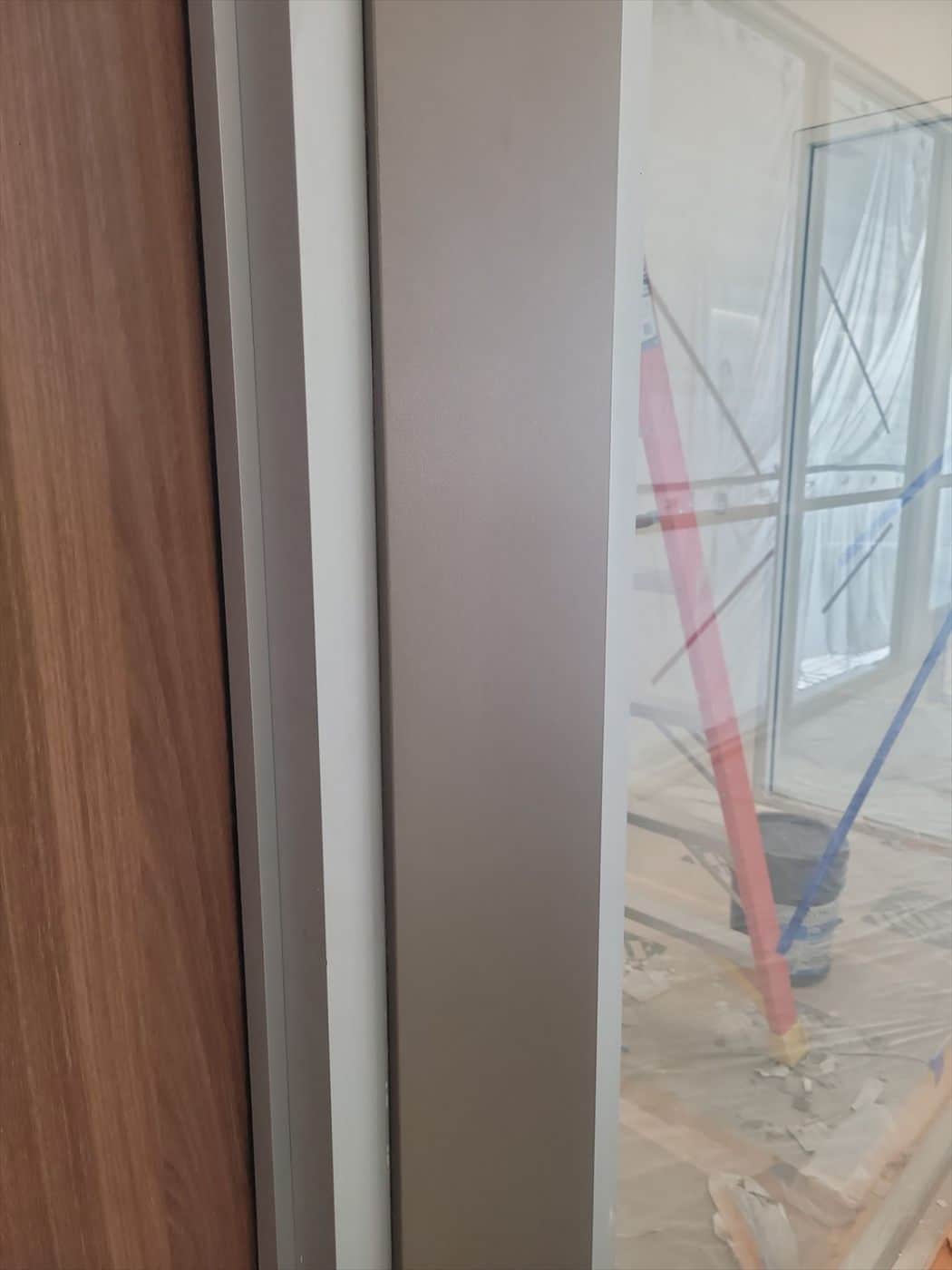 Detail of a wood-panel wall, taupe painted column trim and adjacent glass.