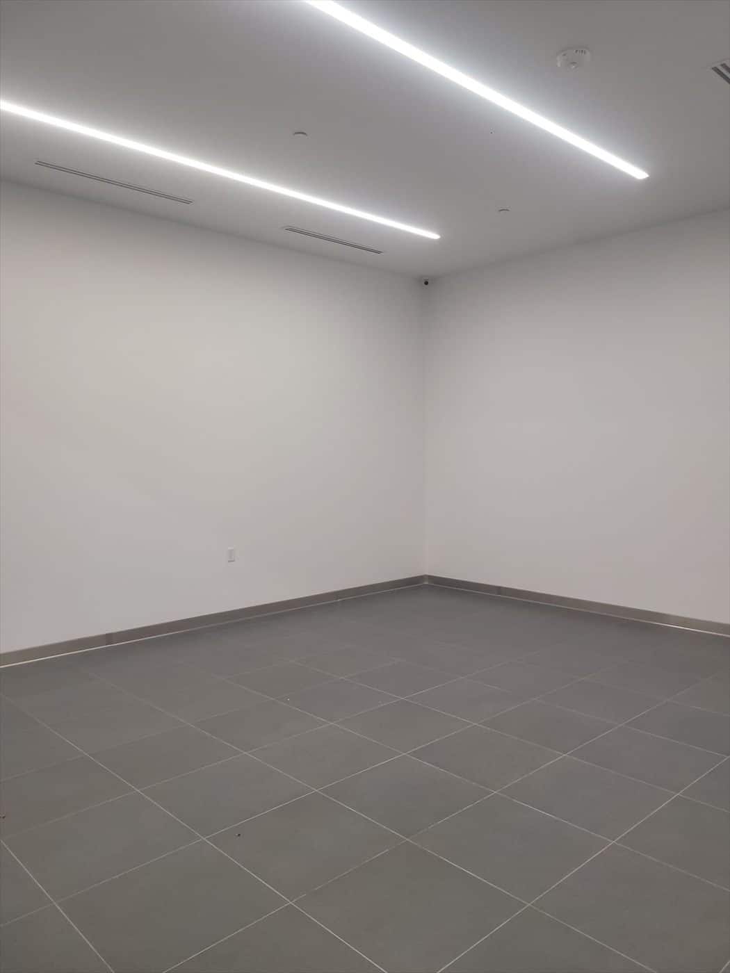 Empty finished office room with white walls, gray tile floor and linear lighting.