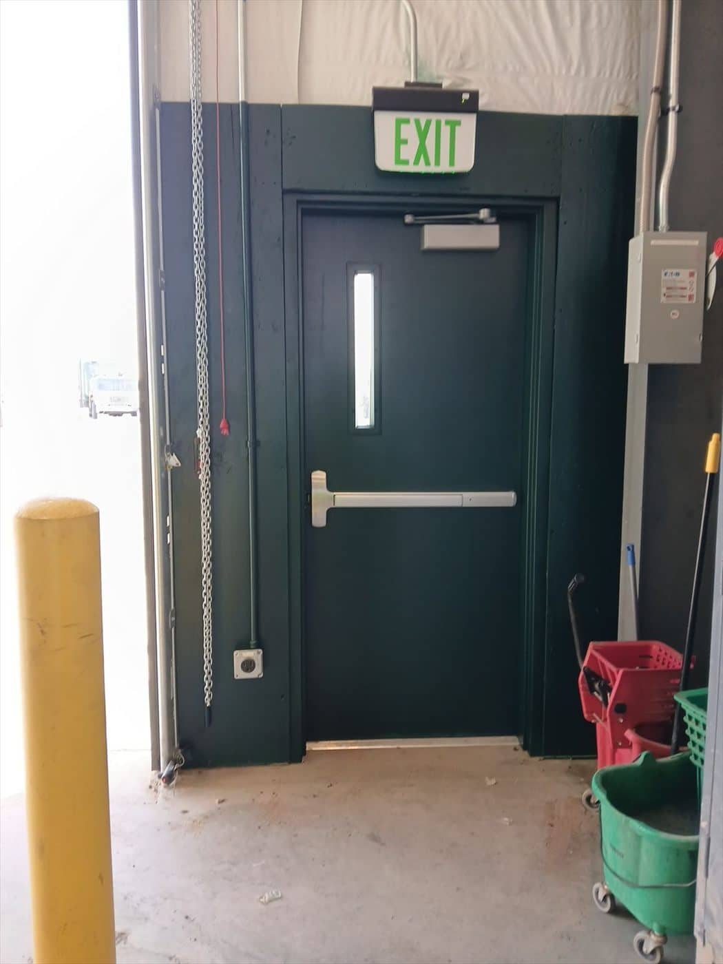 Green painted wall framing an exit door with panic bar and exit sign.