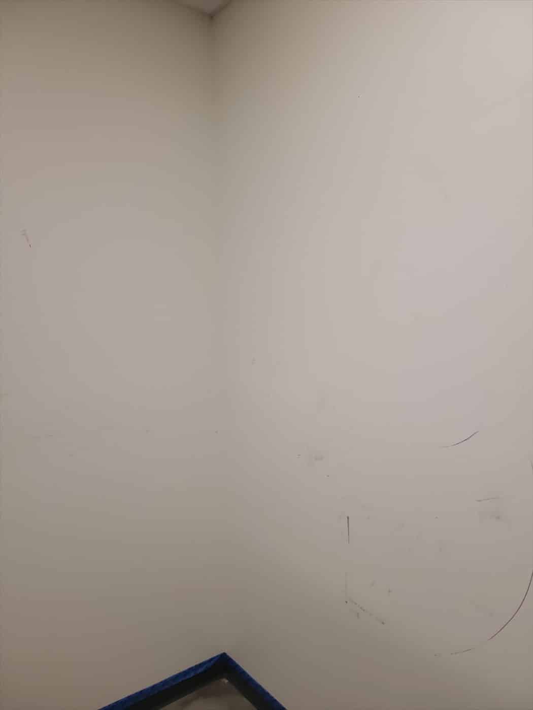 Interior corner walls with marks and taped baseboard before painting.