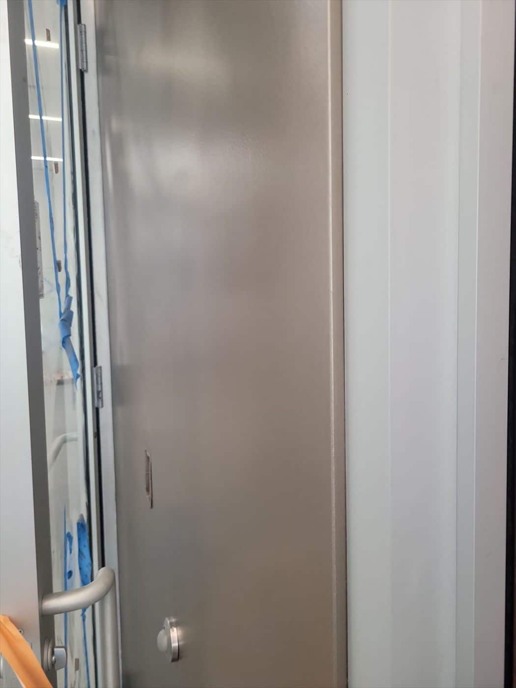 Detail of a stainless steel door panel beside a painted gray wall and trim.