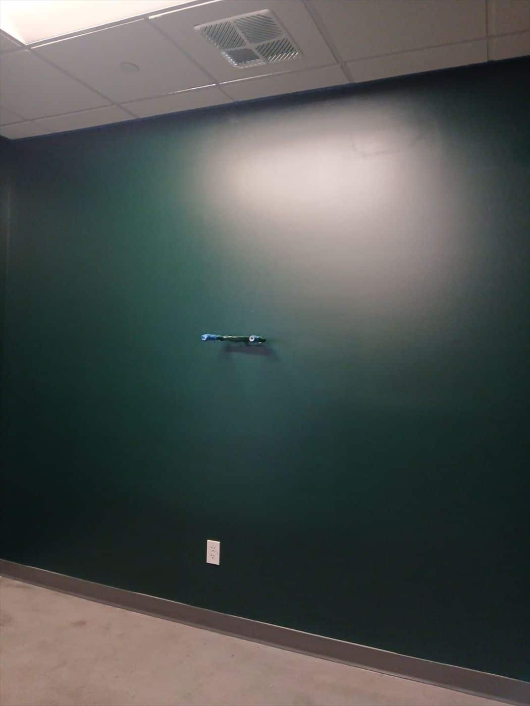 Smooth dark green painted office wall with light switch and vent.