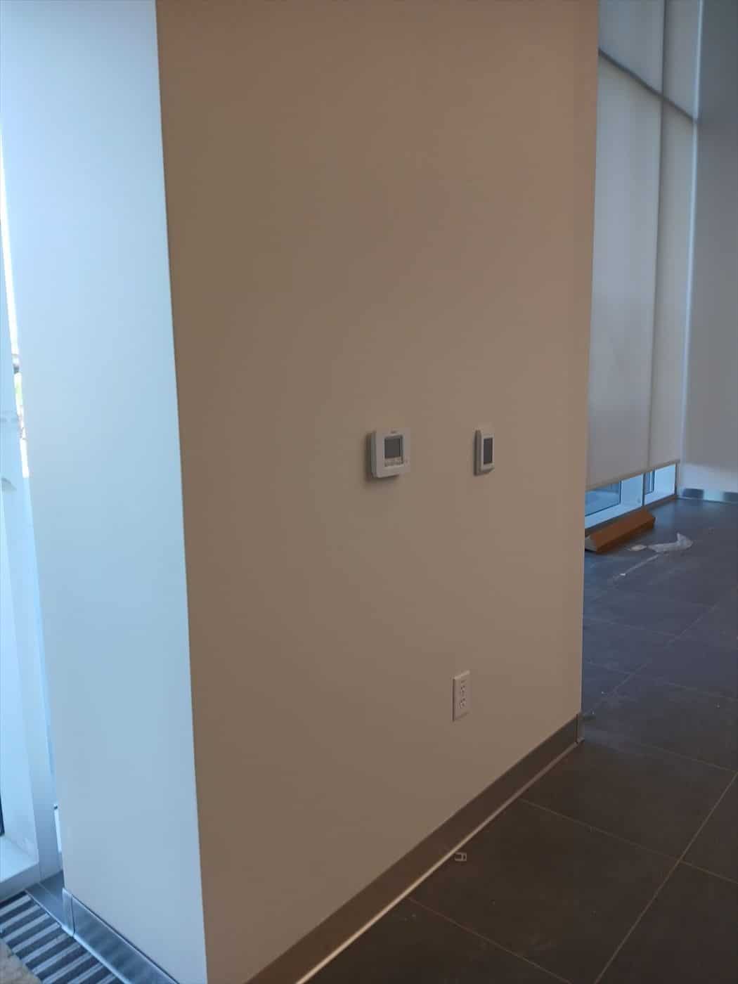 Finished tan accent wall with thermostats above dark tile flooring.