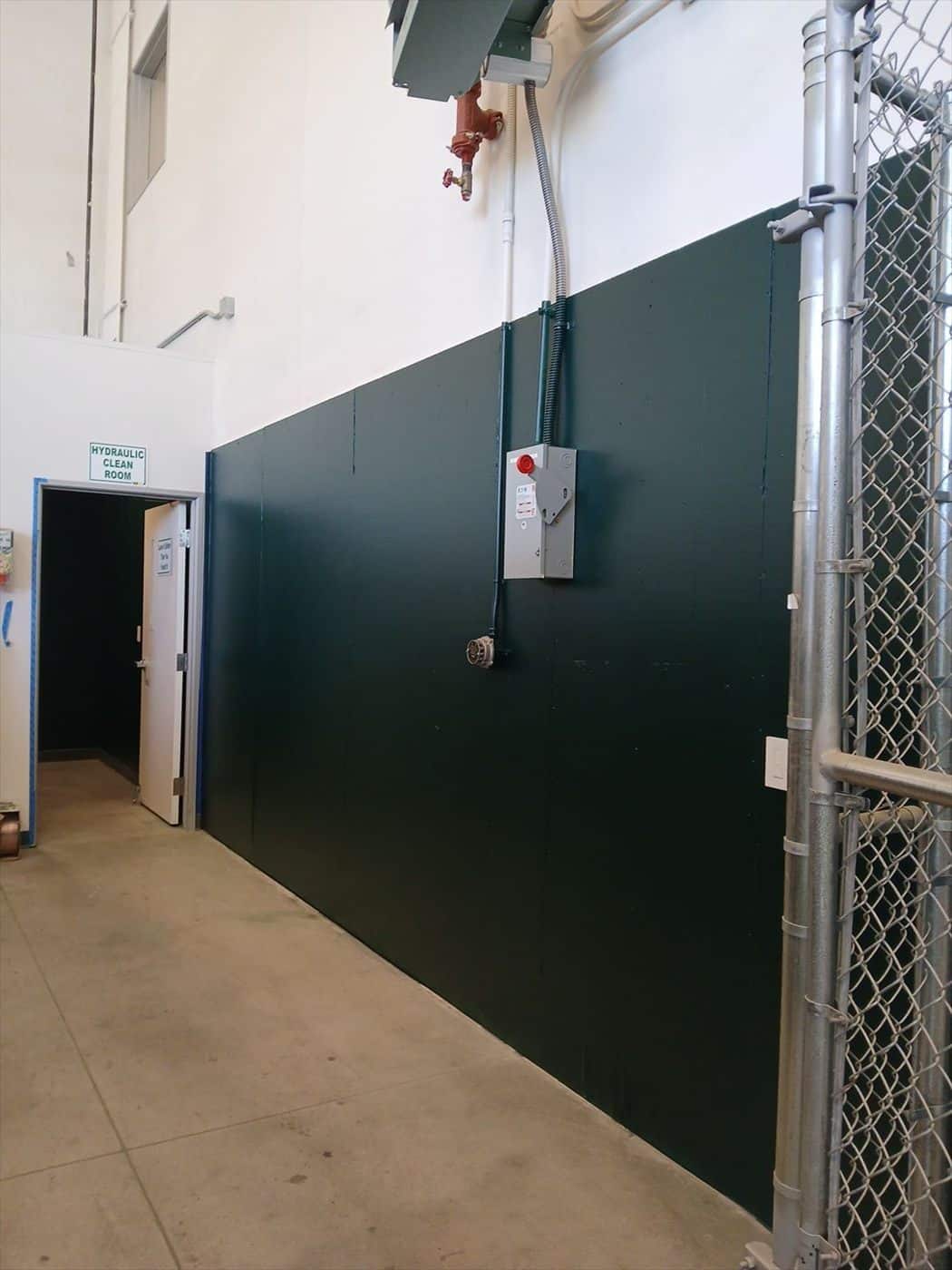 Green painted wainscot wall with electrical box beside a chain-link gate.
