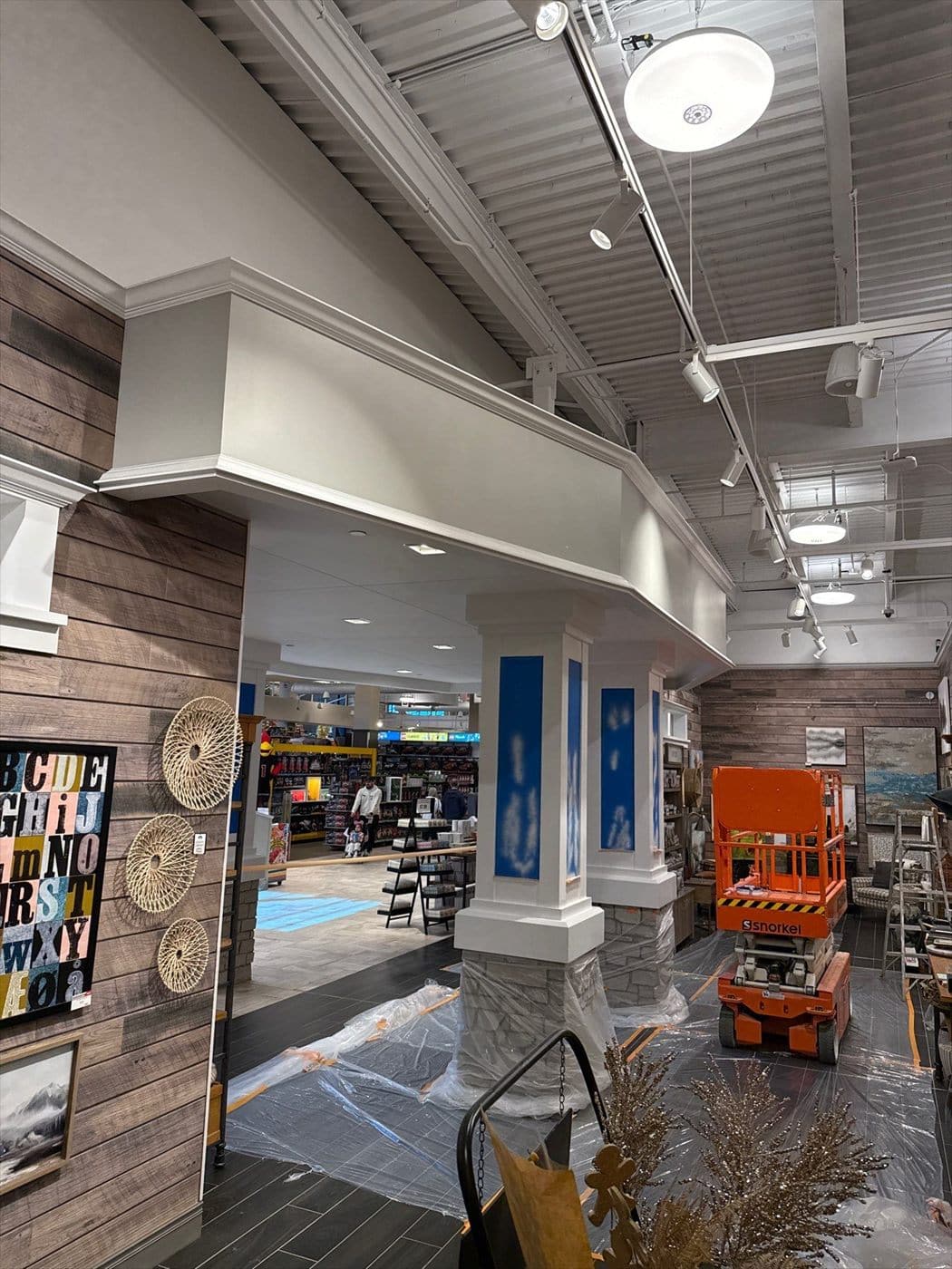 Painted columns and soffit near a wood-plank wall with a scissor lift and floor protection during interior work.
