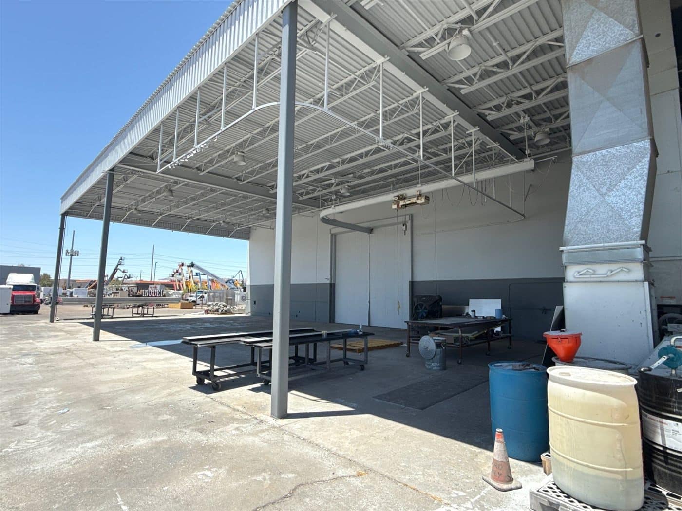 Exterior covered canopy work area with tables and drums against a repainted two-tone wall.