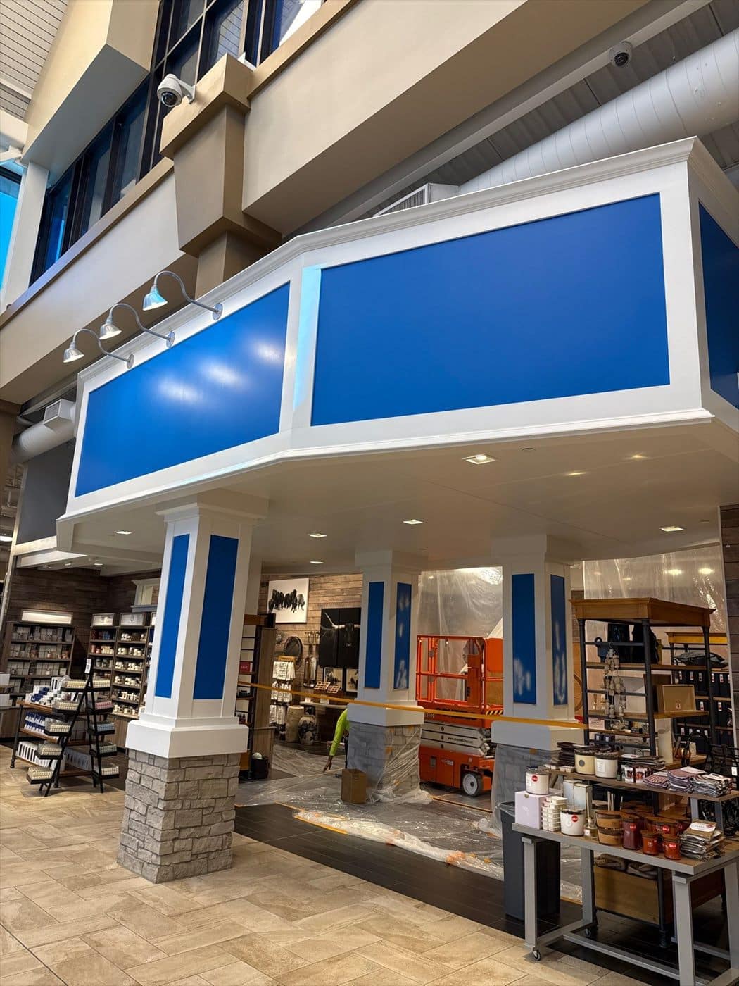 Painted blue-and-white entrance soffit above a department where a scissor lift and containment remain in place.