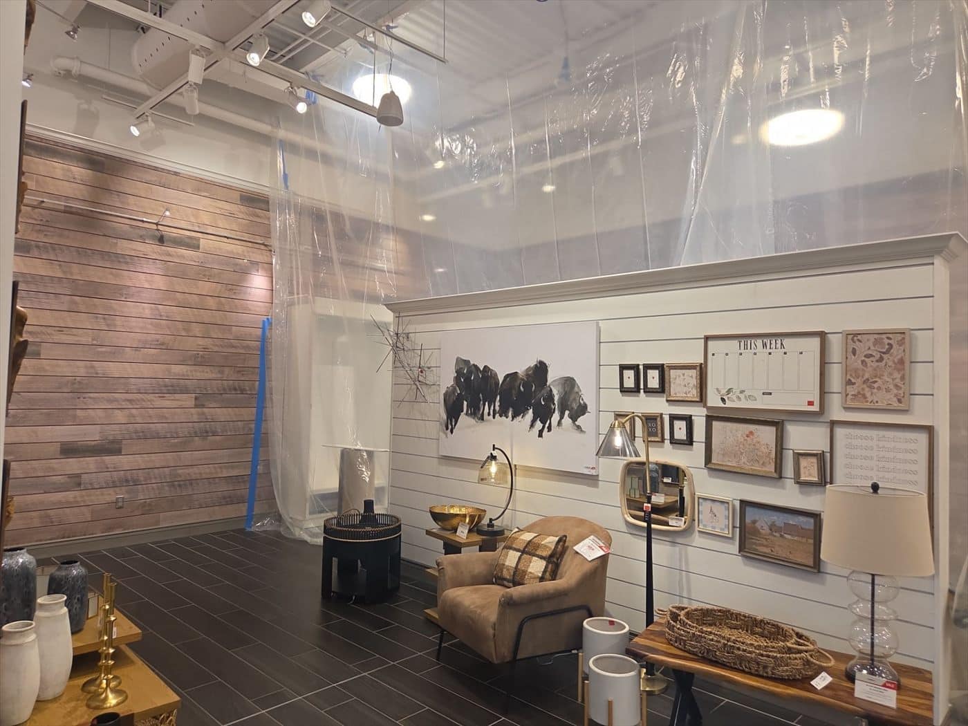 Retail display area with white shiplap gallery wall beside plastic containment sheeting during interior work.