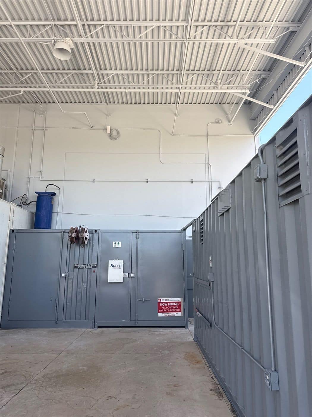 Interior storage enclosure and cabinets painted gray beneath exposed steel roof trusses.