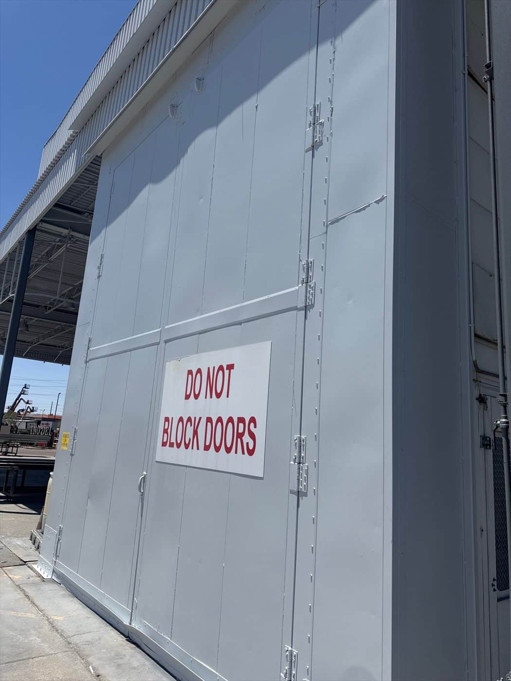 Gray-painted exterior metal enclosure marked with a Do Not Block Doors sign.