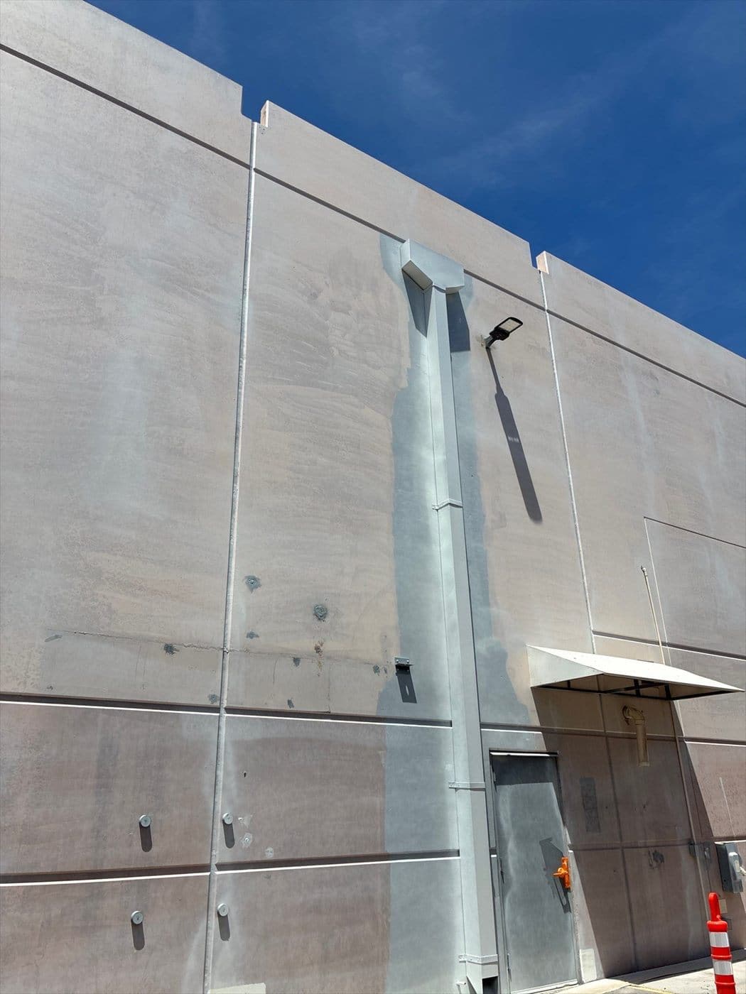 Bare concrete tilt-up wall with downspout awaiting paint against a clear blue sky.