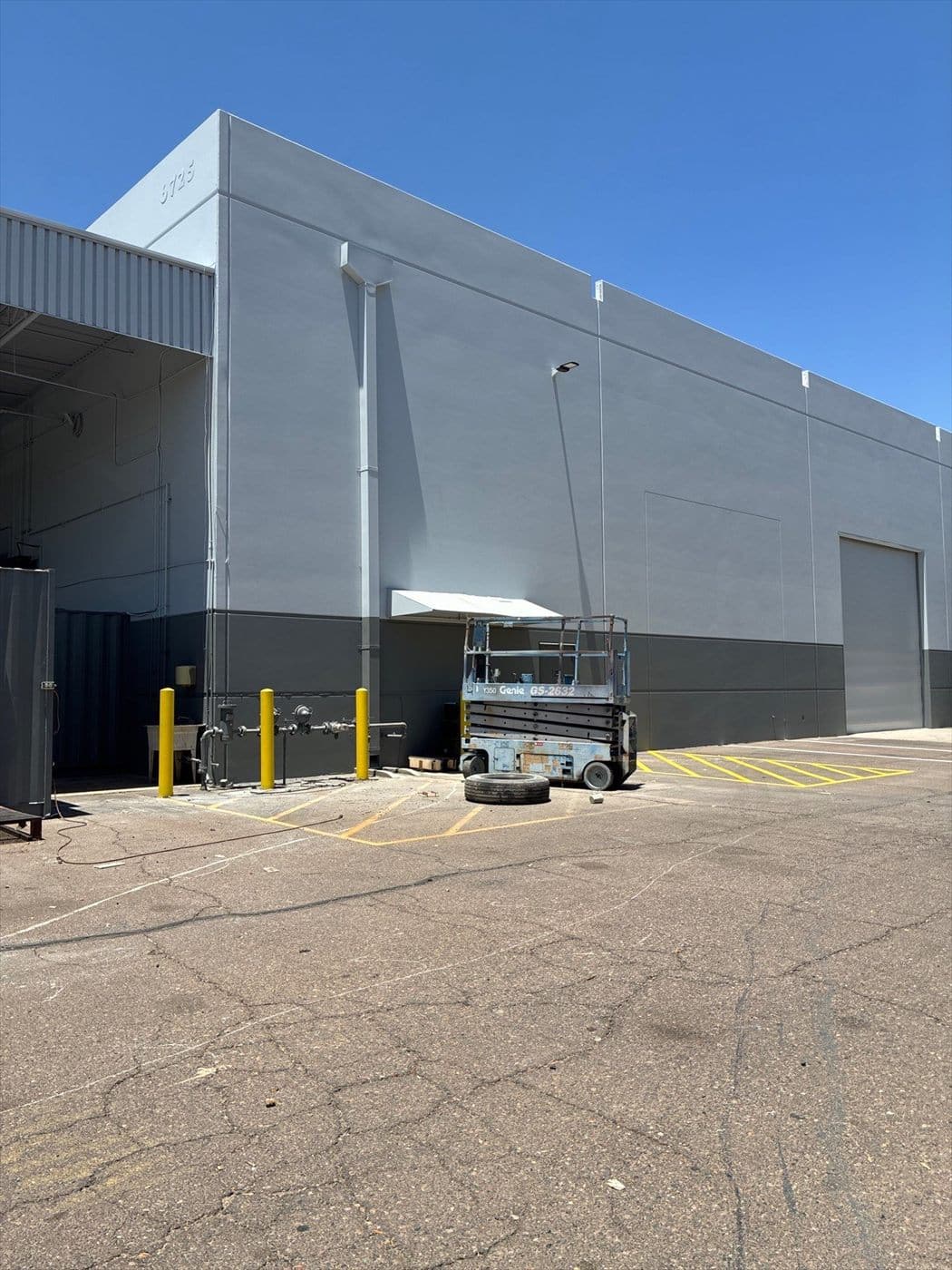 Repainted two-tone warehouse wall with a scissor lift and bollards in the lot.