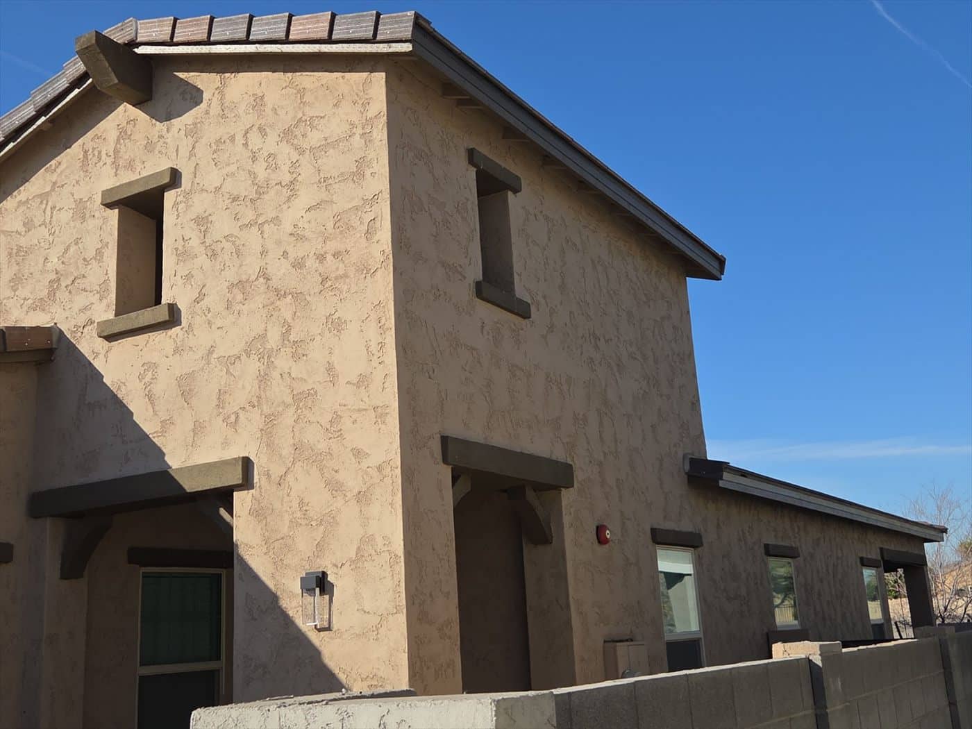 Two-story tan stucco building exterior against clear blue sky.