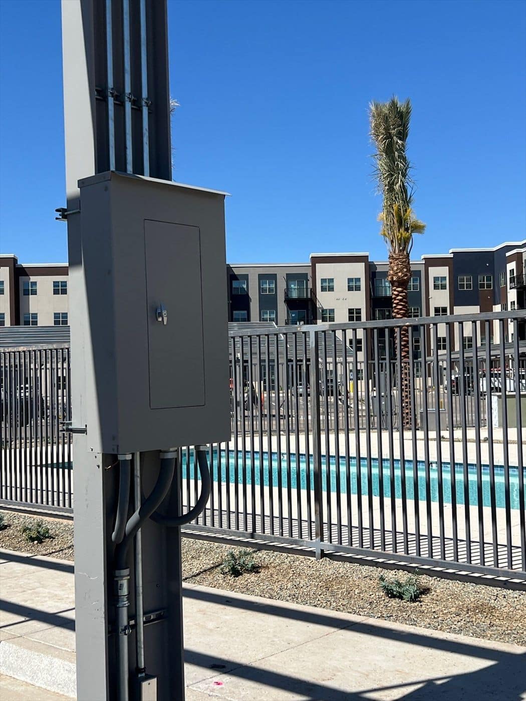 A gray painted electrical box on a carport column with an apartment pool area in the background.