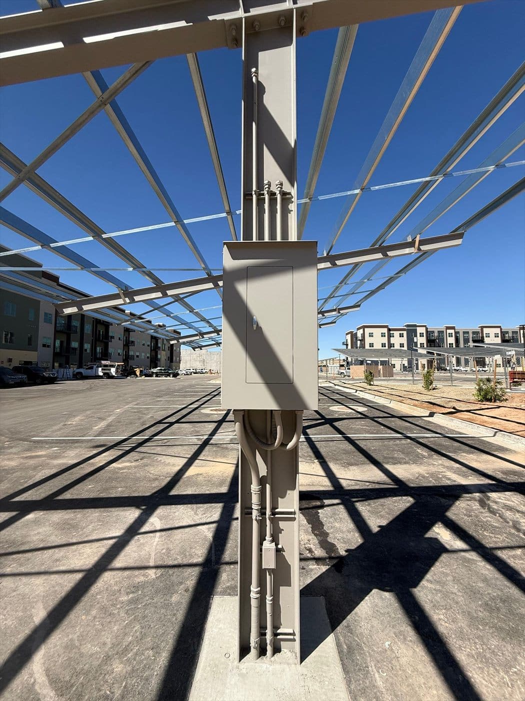 A painted gray electrical box on a carport column casting shadows across the finished parking lot.