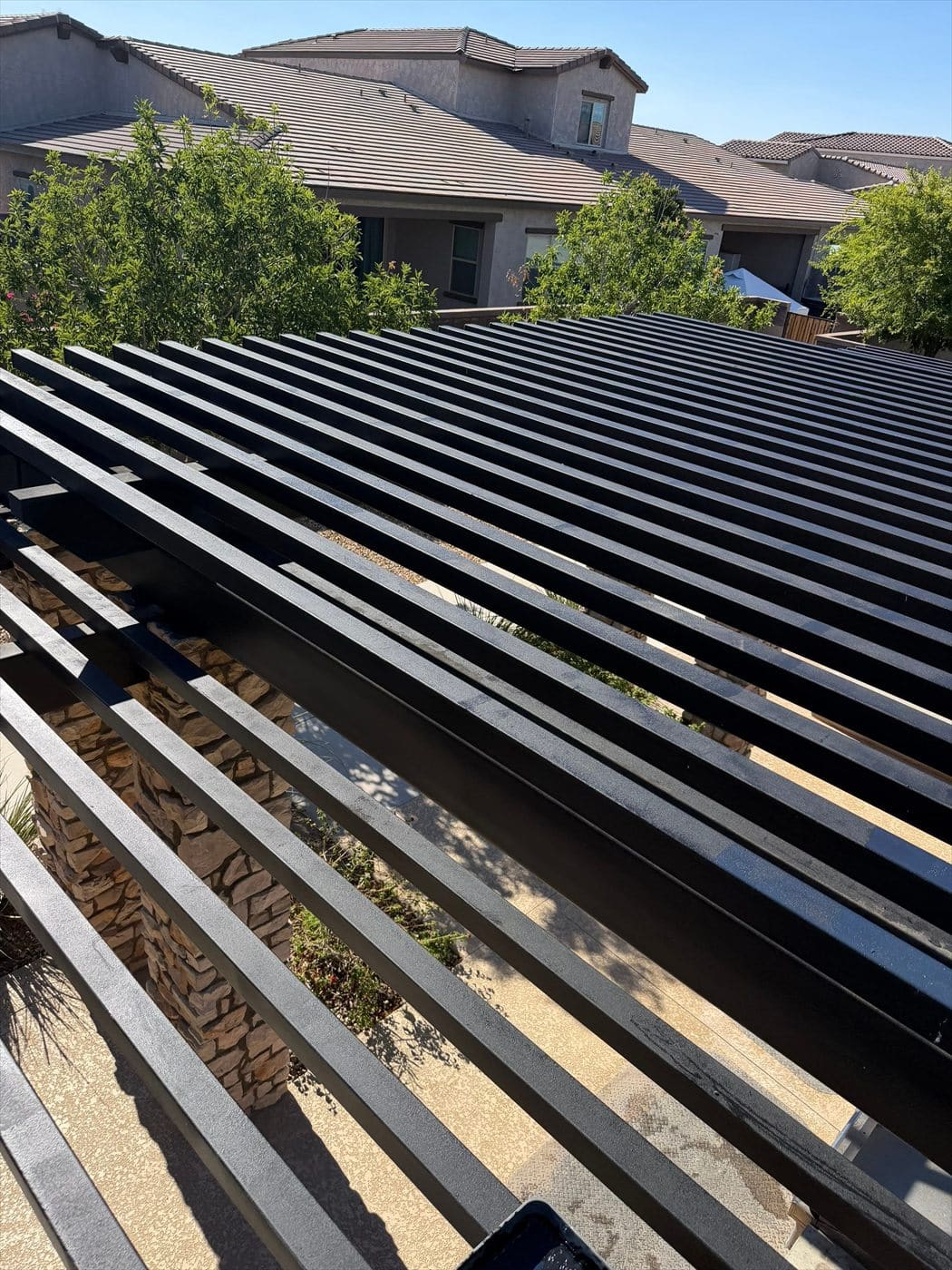 Elevated view of a black metal louvered pergola near community homes.