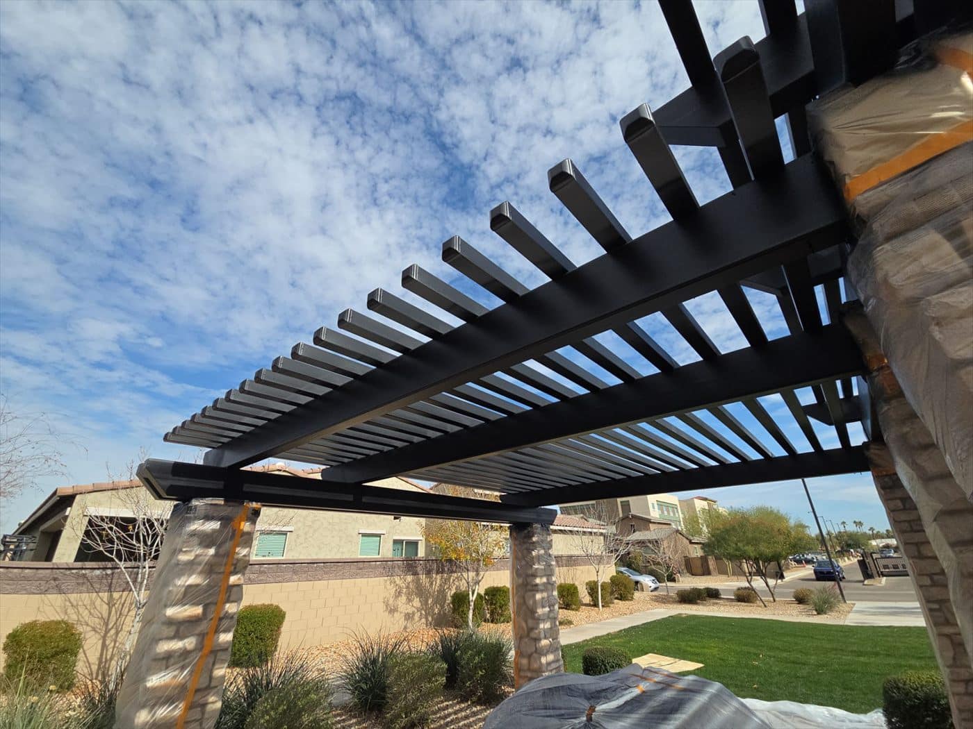 Freshly coated black metal pergola with community buildings in the background.