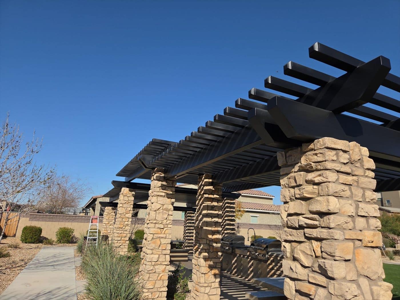 Black metal pergola on stone columns viewed from below against blue sky.