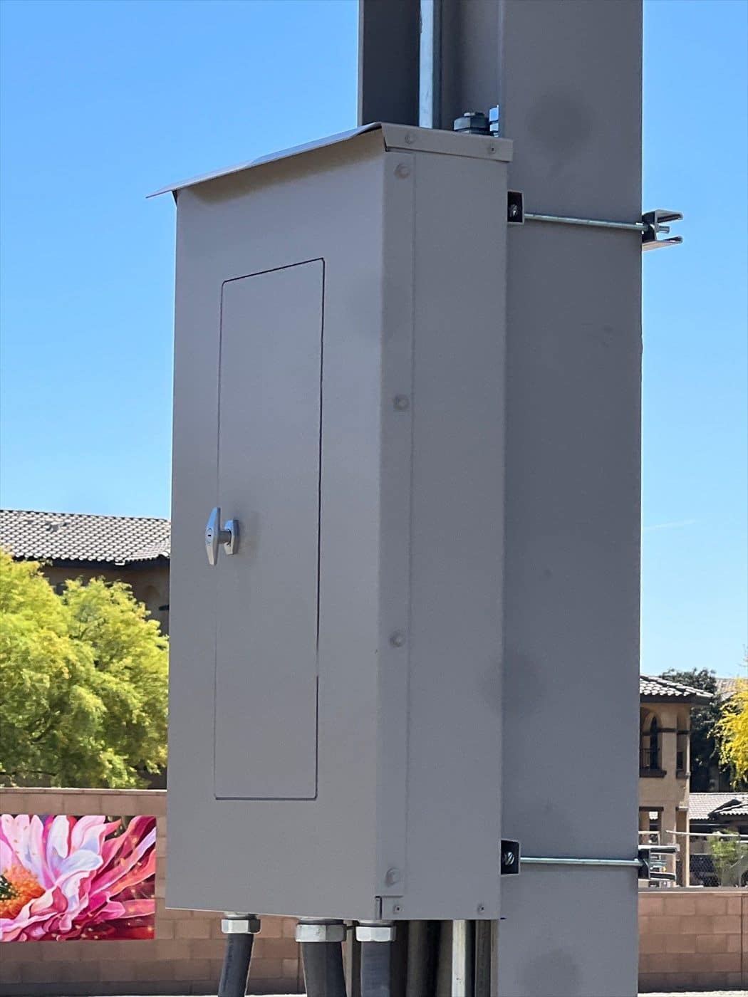 Close-up of a gray painted electrical enclosure mounted on a carport column against a blue sky.