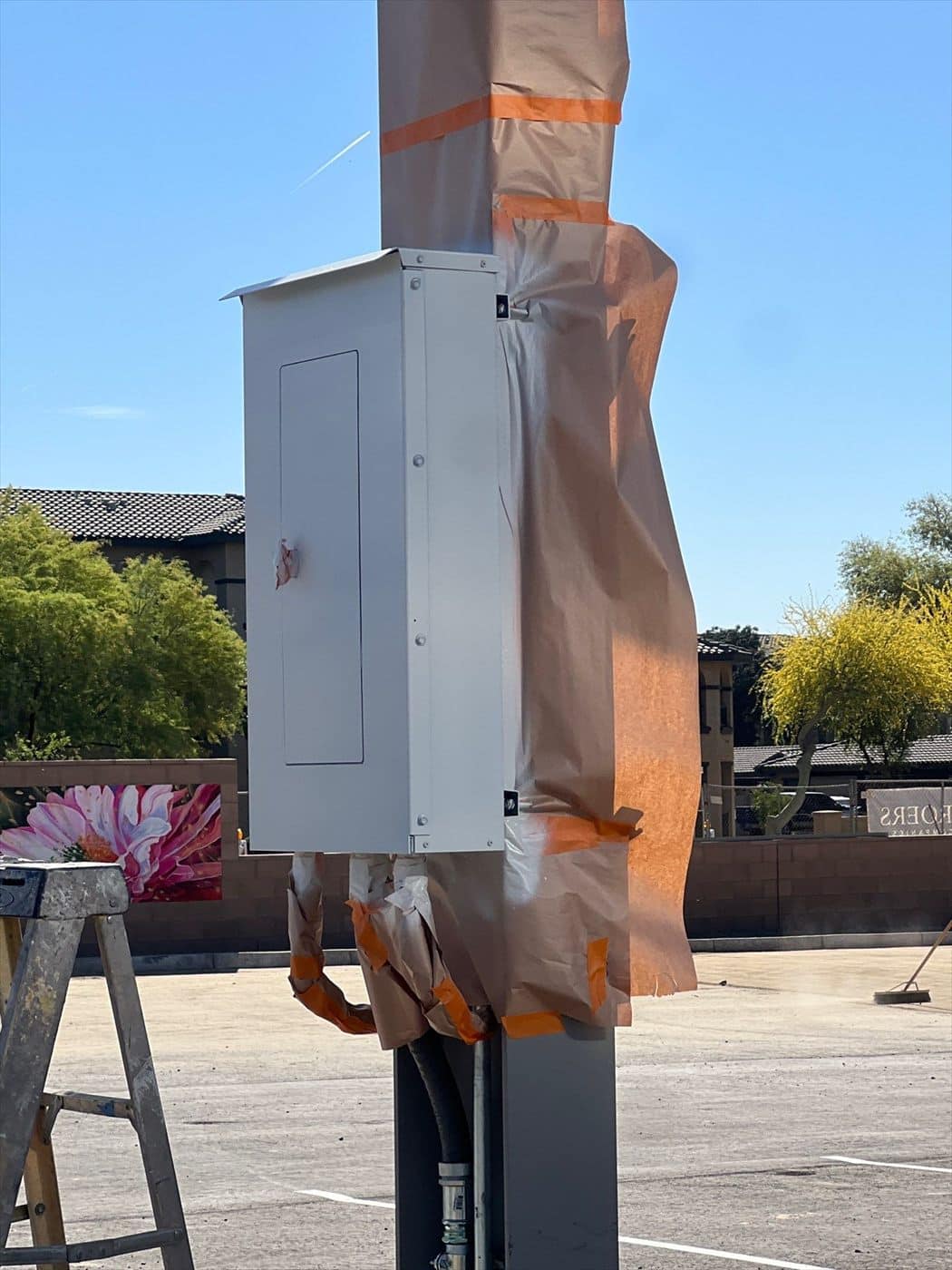 Close-up of a white electrical enclosure with the column above wrapped in paper and orange tape.