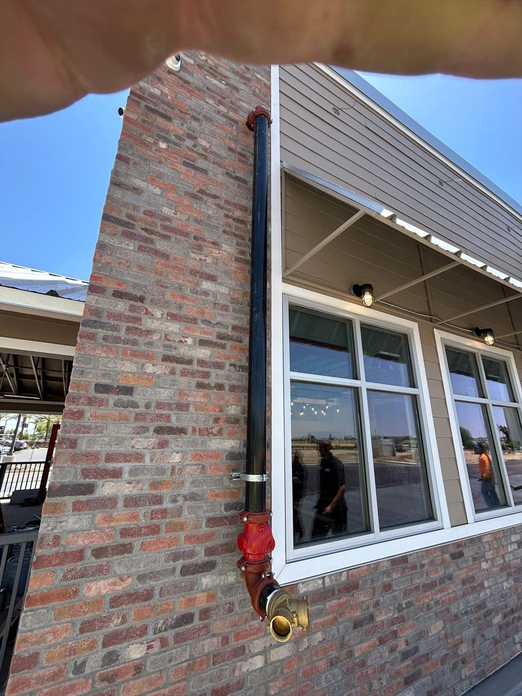 Detail of a brick column corner with a painted downspout and windows reflecting the parking lot.
