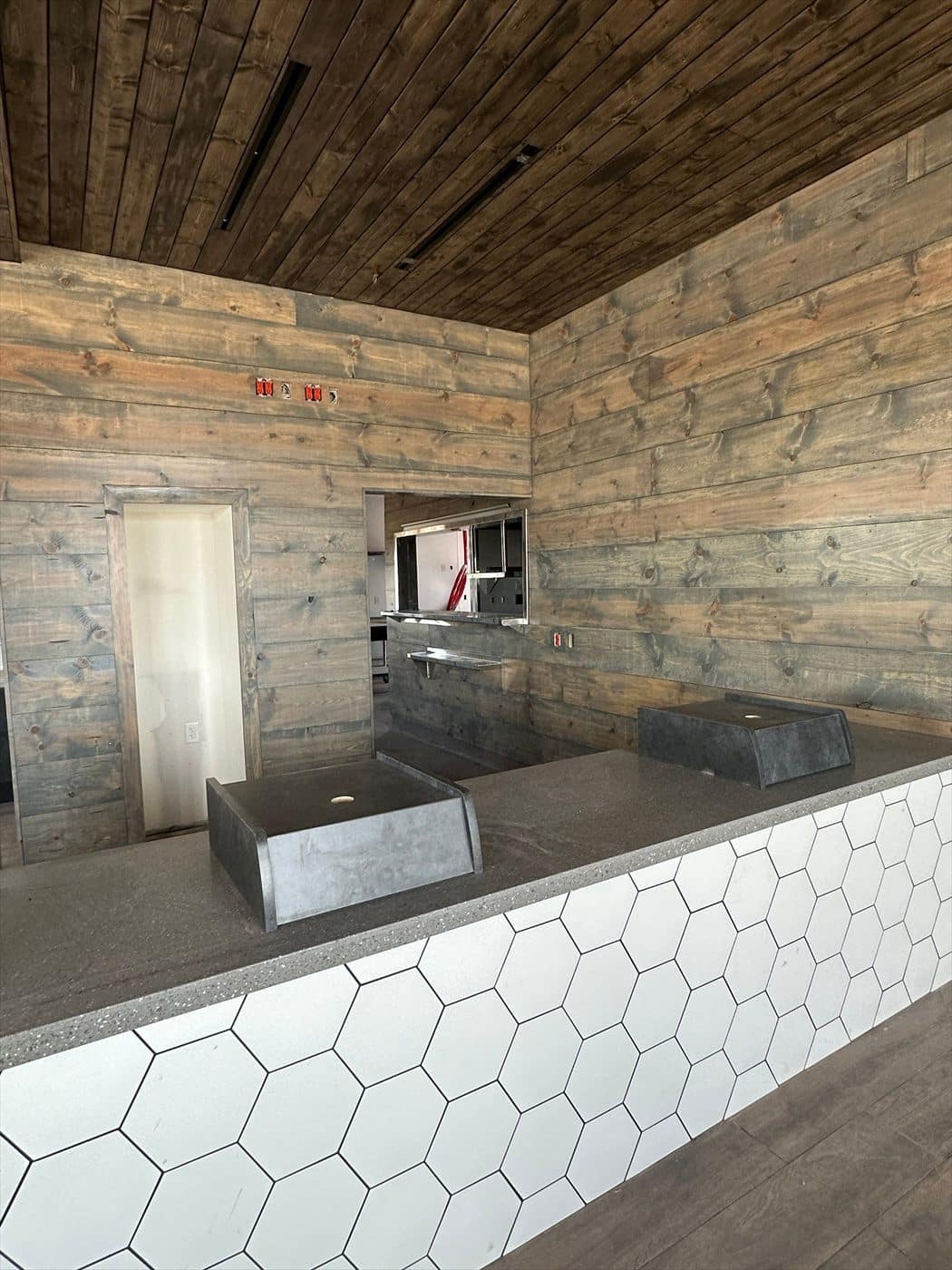 Finished counter area with white honeycomb tile front, wood plank walls, and a view into the kitchen.