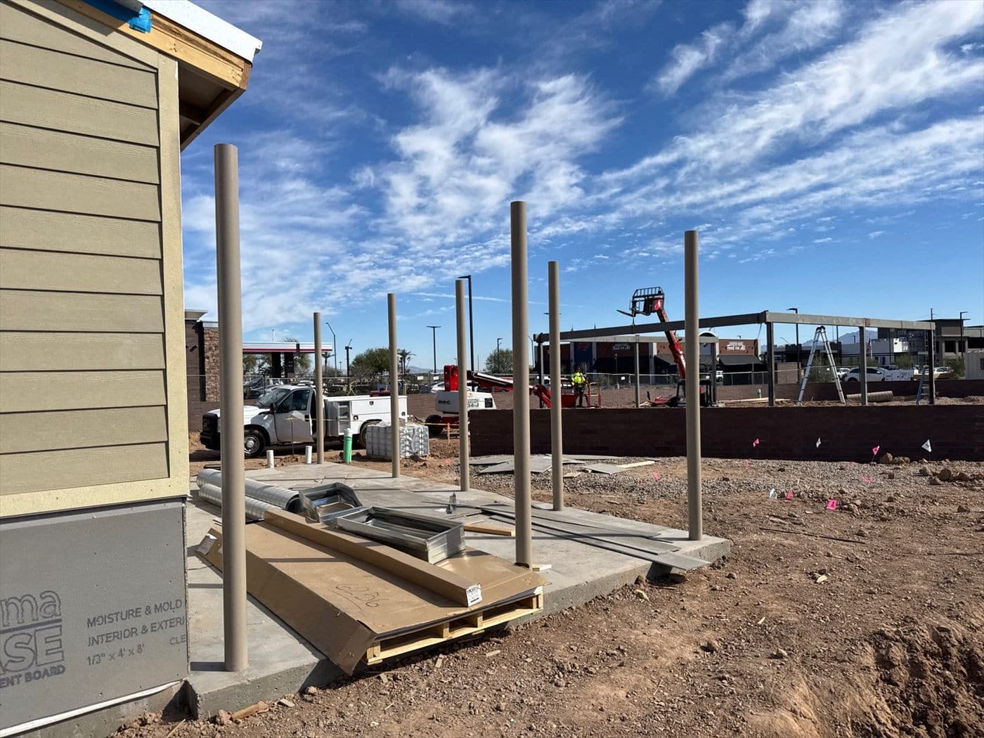The building corner early in construction with steel posts and moisture-resistant board exposed against a blue sky.