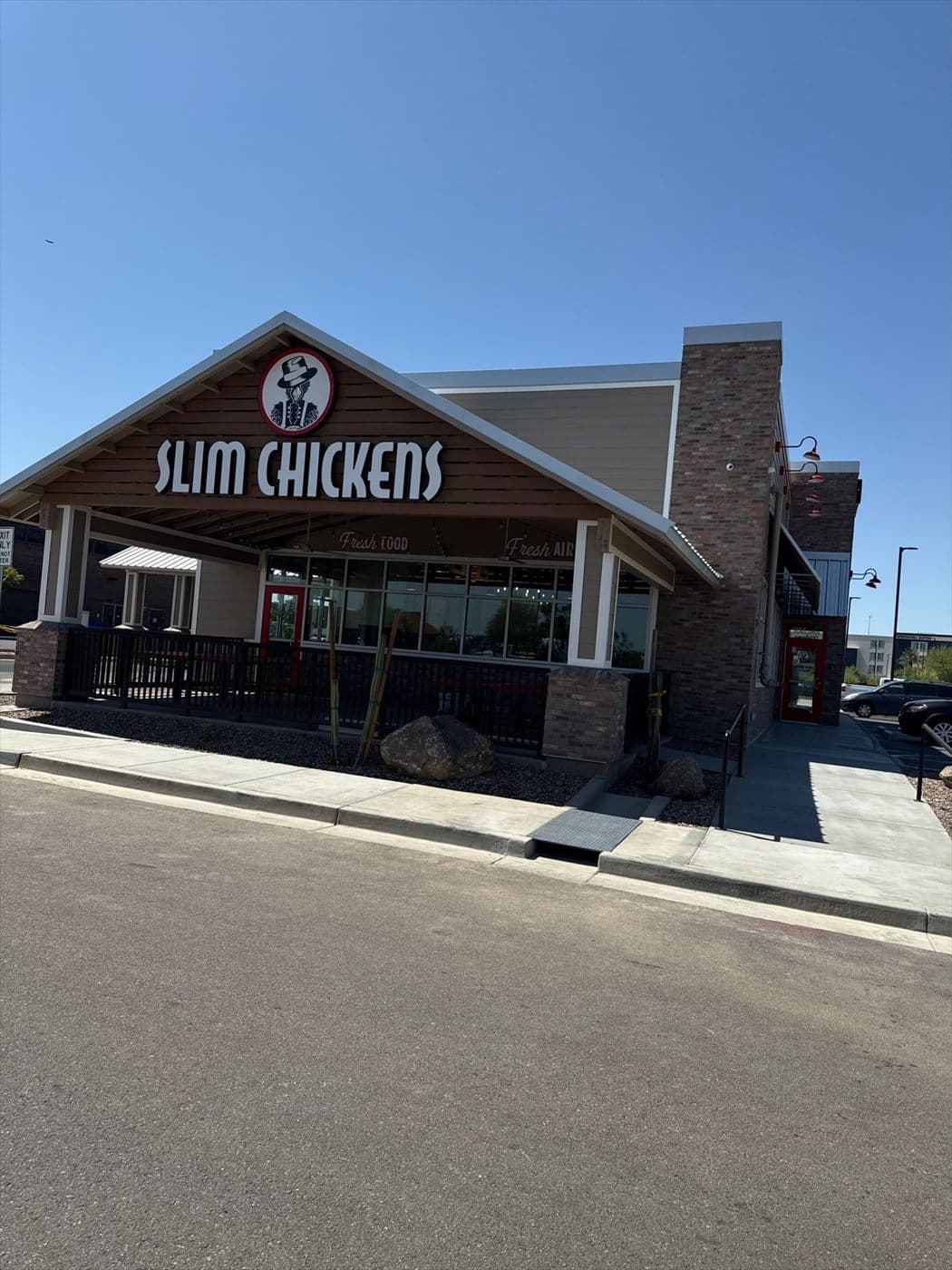 The completed front entrance of the Slim Chickens restaurant with brick, signage, and covered patio.