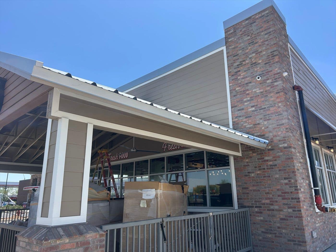 Exterior side view of the covered patio with metal roof, tan soffit, and brick column.