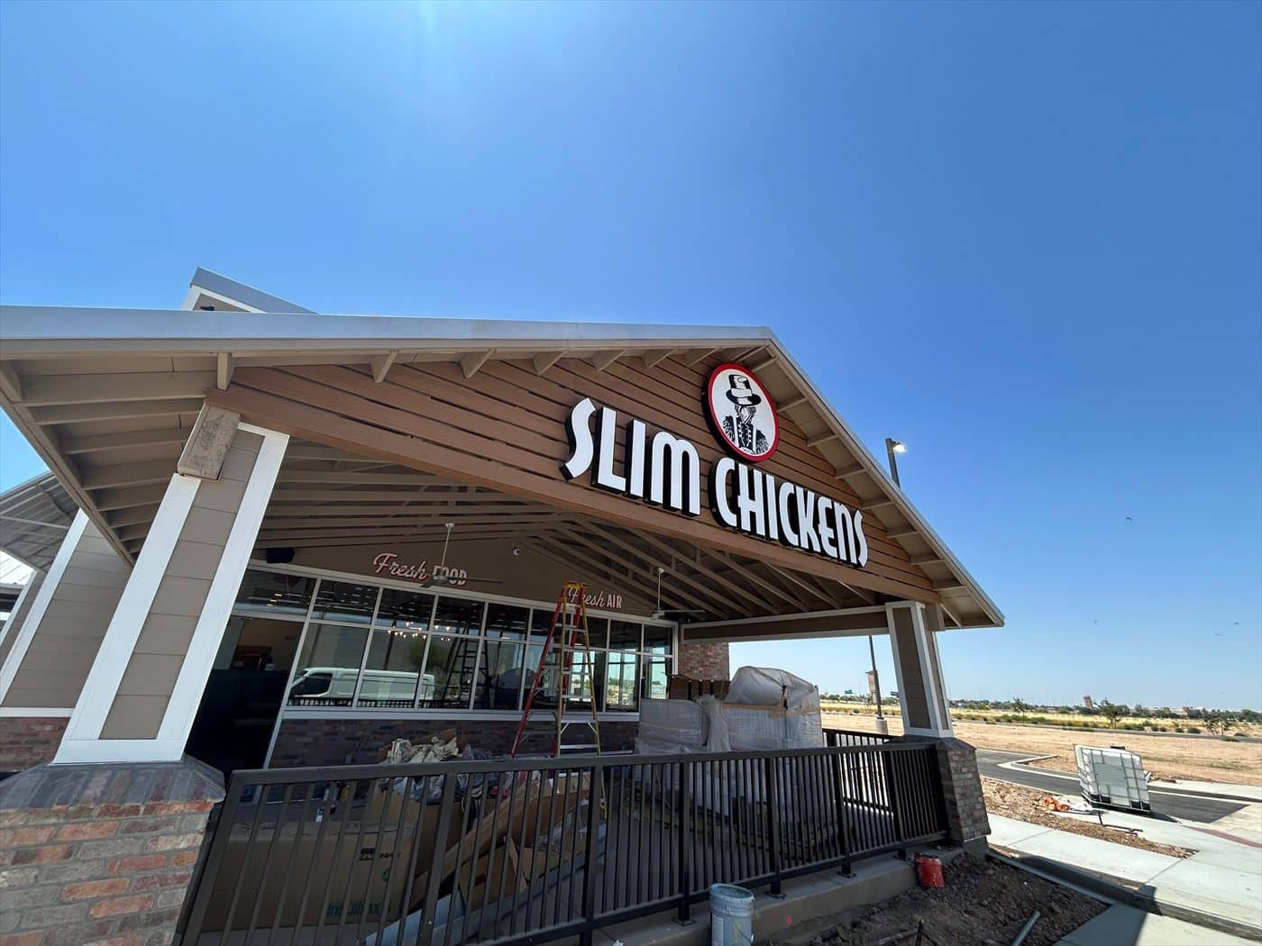 The illuminated 'Slim Chickens' sign and logo mounted on the finished entry canopy above brick and siding.