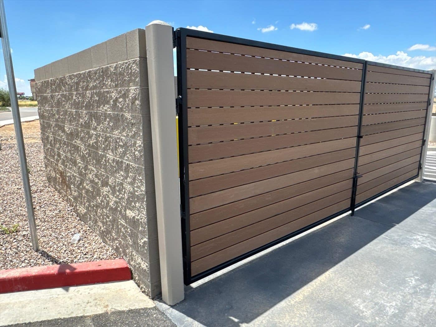 A completed trash enclosure with brown composite gates and a split-face block wall.