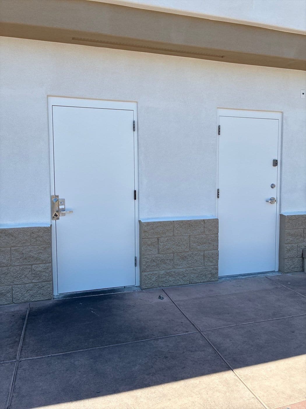 Two freshly painted white exterior doors on a stucco wall with block wainscot.