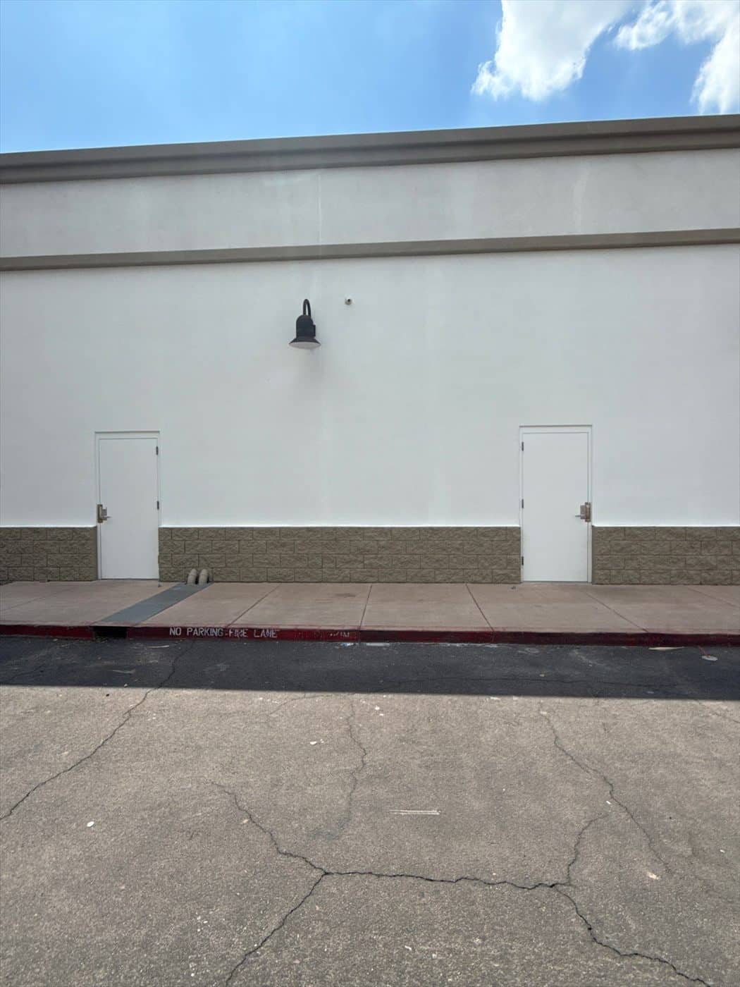 Finished exterior wall with two painted doors, a sconce, and fresh fire-lane striping.