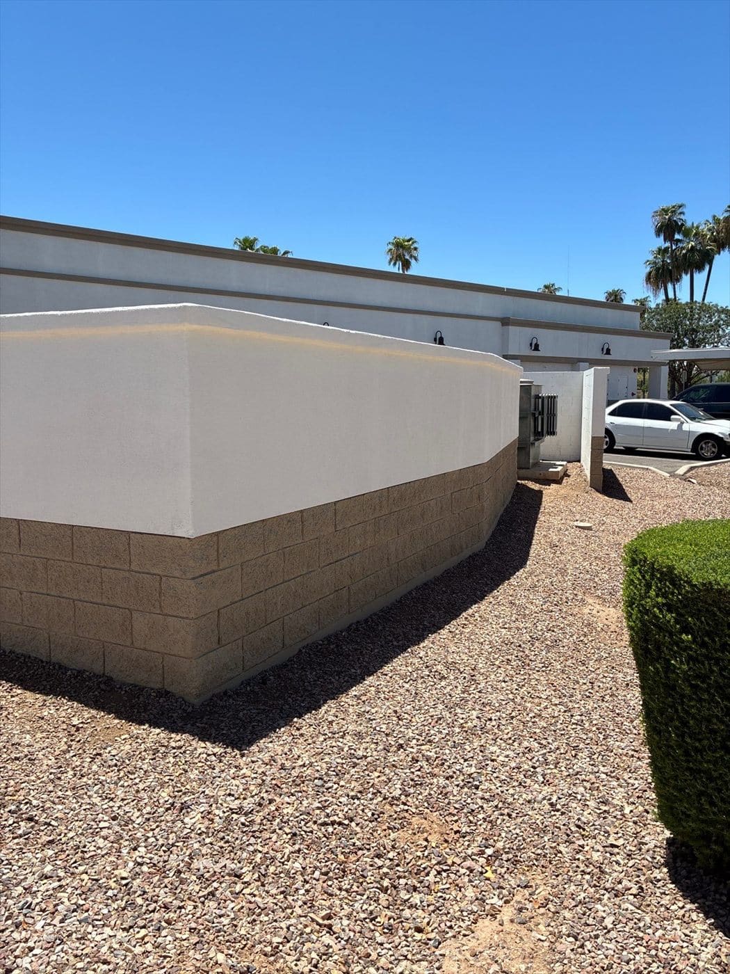 Painted exterior wall corner with block wainscot above a gravel landscape bed.