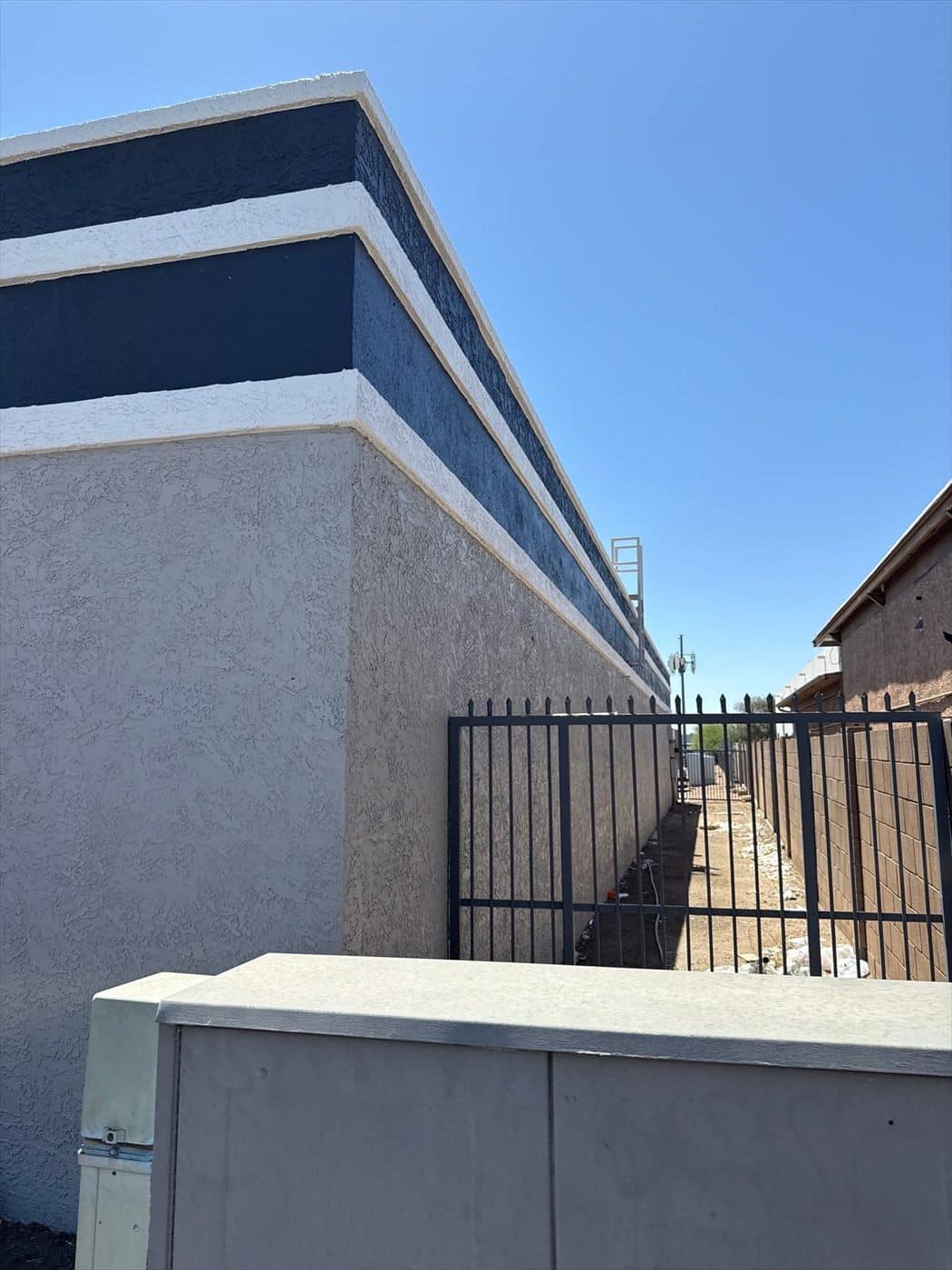 Completed parapet showing the crisp navy-and-white banding above the gray wall behind a fence.