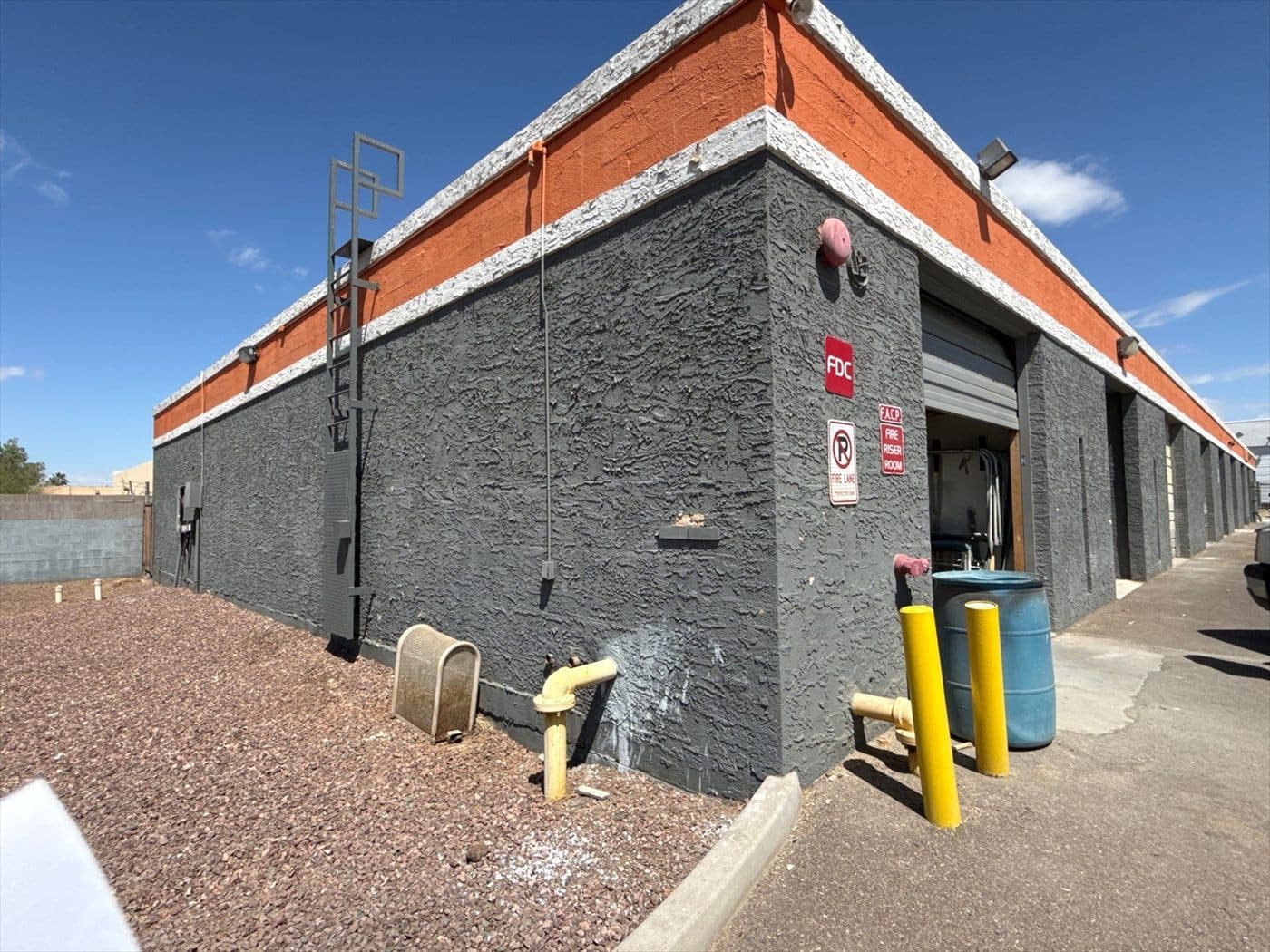 Building corner with gray stucco and faded orange band prior to surface prep and painting.