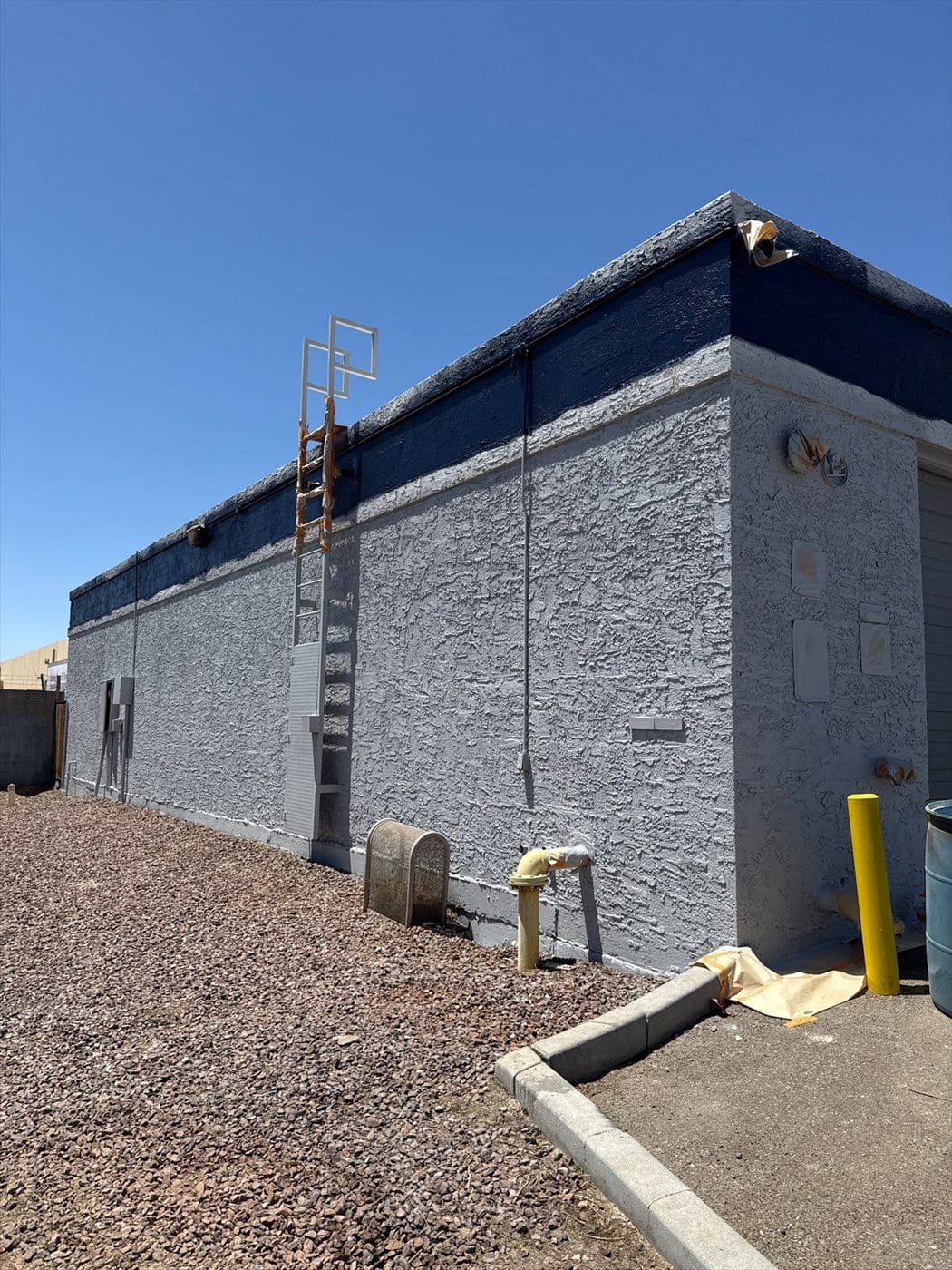 Finished exterior wall in gray with navy parapet band and a fixed roof access ladder.