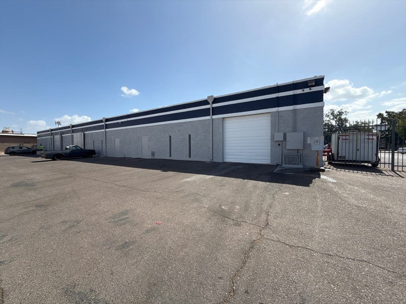 Long side elevation of the warehouse finished in gray with a navy accent stripe and white roll-up door.