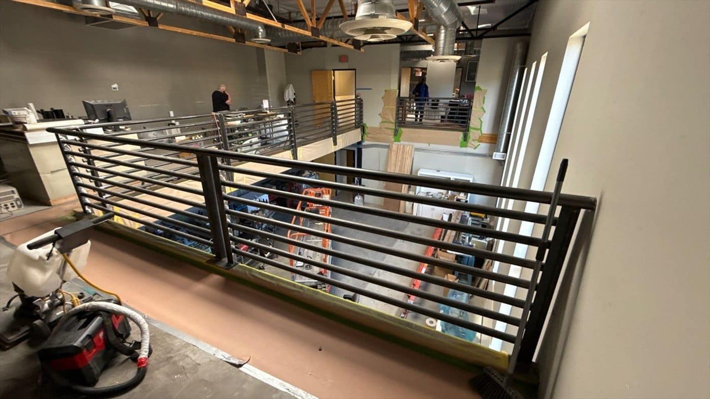 Unpainted metal mezzanine railing in an open commercial interior before coating work begins.