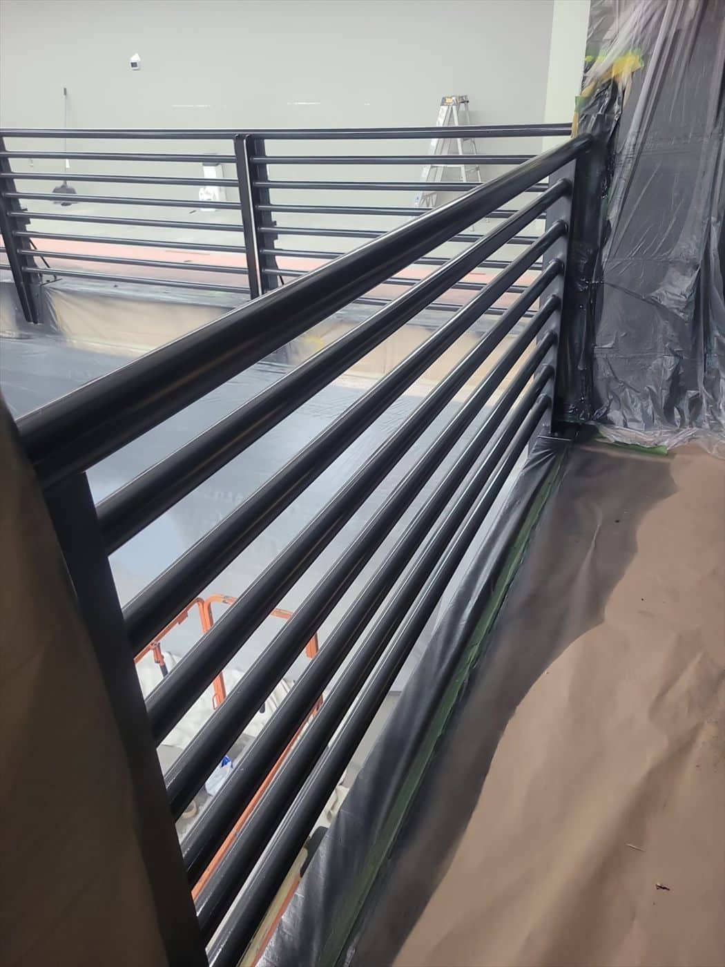 Black-coated horizontal-bar mezzanine railing over masked flooring.