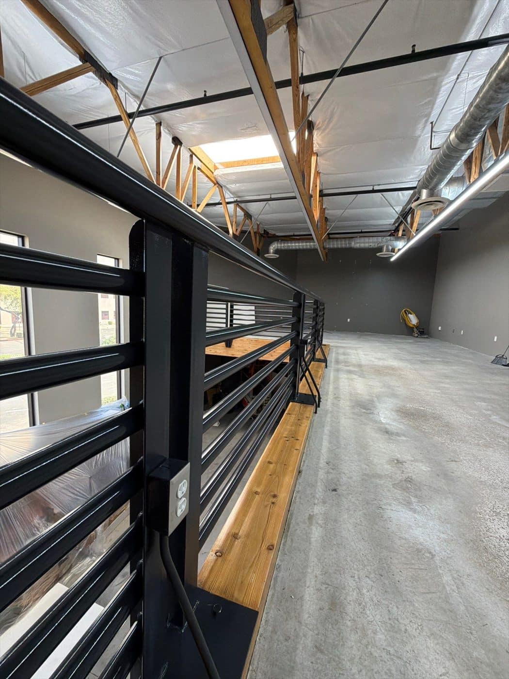 Finished black mezzanine railing running along the open commercial floor.