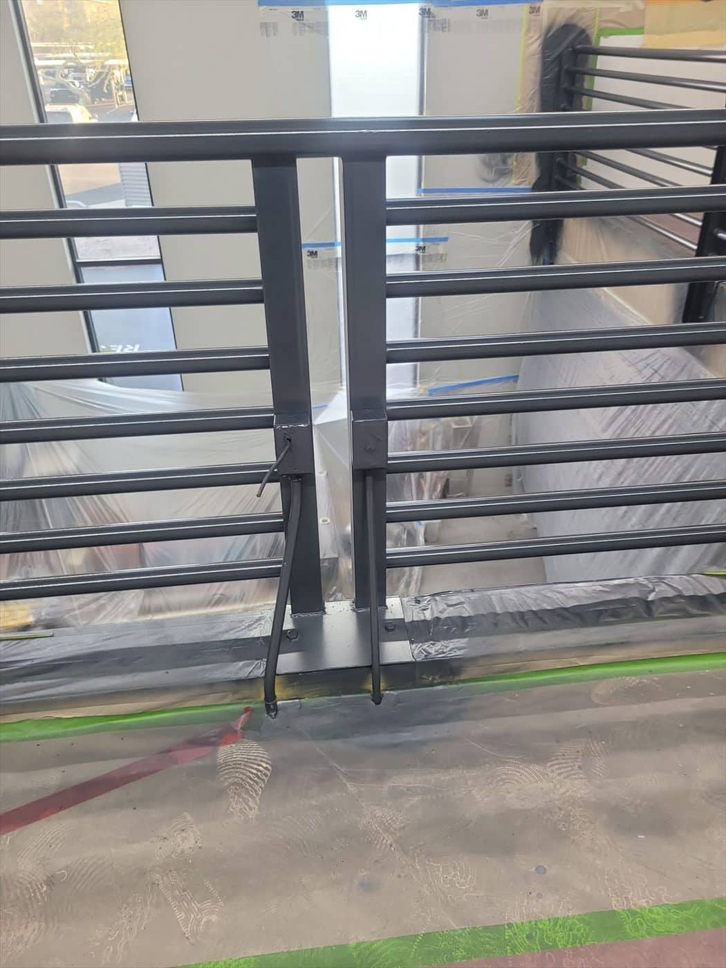 Detail of a black-coated railing post and mounting base above masked floor.