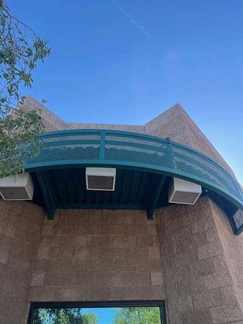 Curved teal-green painted metal canopy and screen wrapping a split-face block building corner.