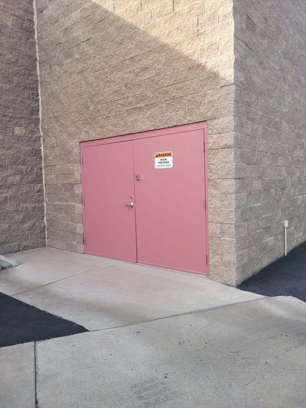 Pink painted double doors with high-voltage warning signage in a block wall.