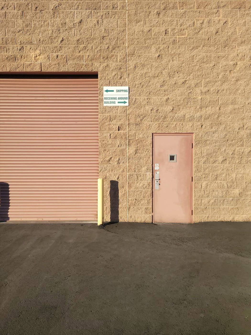 Peach painted rolling door and personnel door with shipping-and-receiving signage on a block wall.
