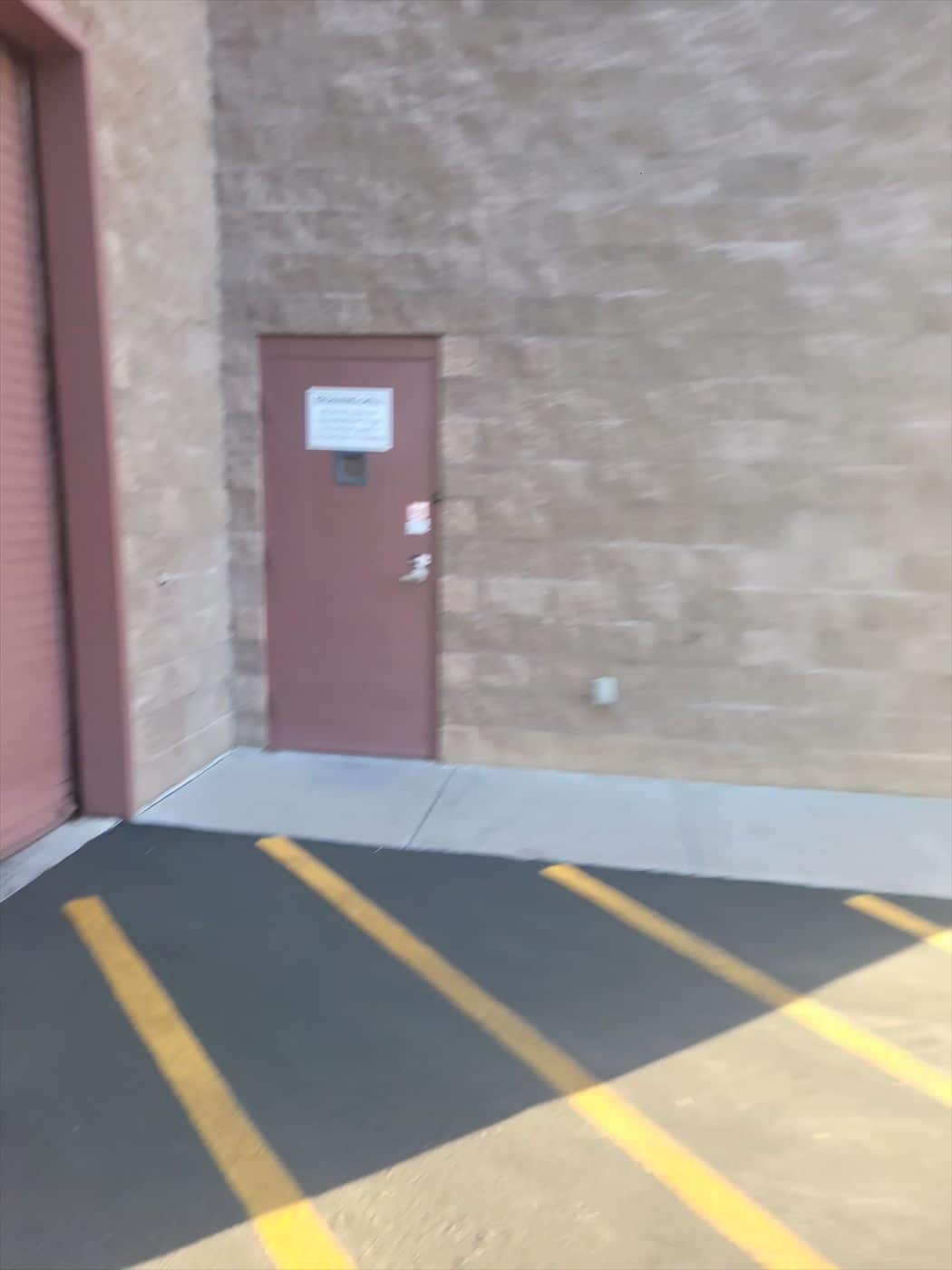 Maroon painted personnel door on a block wall beside a rolling door and striped parking lot.